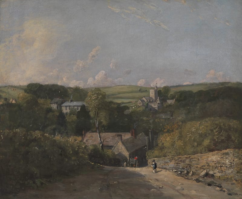 A lane running down into a village among trees, with a church tower and green downland behind.